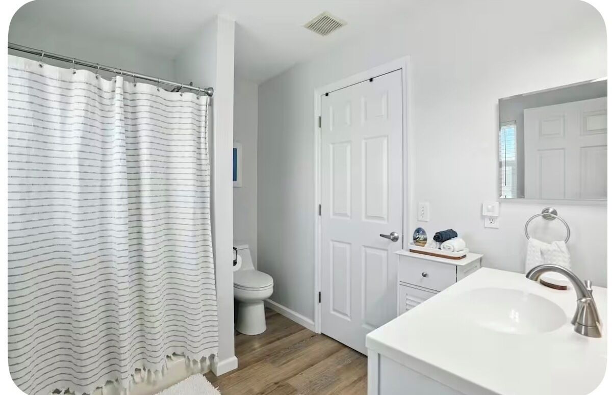 Baño con cortina de ducha, inodoro, lavabo y puerta con toallero.