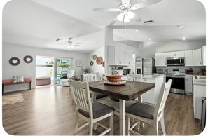 A modern kitchen with white cabinets, a dining table with chairs, and a ceiling fan. - Nice 3-2 house with AC, heated pool in Cape Coral, near downtown and marinas (Cape Coral)