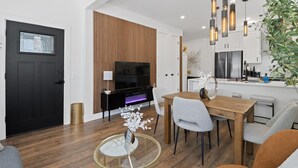Un soggiorno moderno con una porta nera, una parete d'accento in legno, una TV e un'area pranzo con tavolo in vetro.