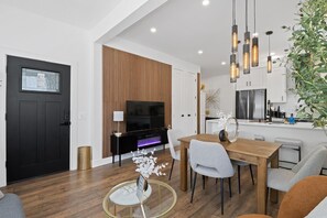 A modern living room with a black door, a wooden accent wall, a TV, and a dining area with a glass table. - Modern Jersey City Duplex with Laundry/ Access to PATH & NYC (Jersey City)
