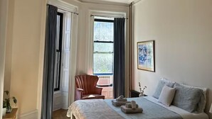 Un dormitorio con cama, una silla, una mesa y un ventanal.