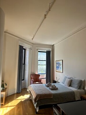 Ein Schlafzimmer mit Bett, Sessel, Tisch und Fenster.
