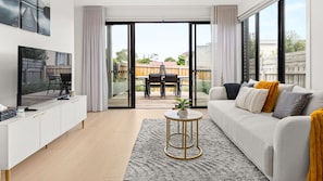 A modern living room with a sofa, TV, and a view to an outdoor patio area. - Fleetwood Atelier Pet Friendly in Frankston South (Frankston South)