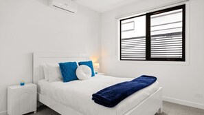 Een slaapkamer met een bed, een witte nachtkastje en een raam met zonwering.