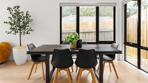 Un área de comedor con una mesa de madera oscura, sillas negras y una planta en maceta.