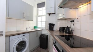 Une cuisine de taille réduite équipée d’un lave-linge, d’une poubelle, d’une cuisinière et d’une fenêtre.