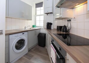 Eine kleine Küche mit Waschmaschine, Mülleimer, Herd und Fenster.