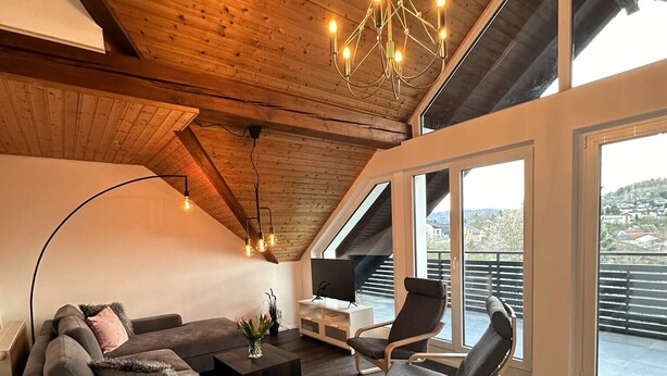 A modern loft with a sloped ceiling, a large window, a sofa, a coffee table, and a chair. - Beautiful modern apartment - Odenwald-Panorama (Reichelsheim (Odenwald))