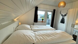 A bedroom with two beds, a window with curtains, a radiator, a potted plant, and a deer head decoration. - Beautiful modern apartment - Odenwald-Panorama (Reichelsheim (Odenwald))