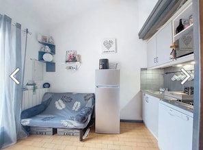 A compact living space with a sofa, a refrigerator, a kitchen area, and a wall with decorative items.