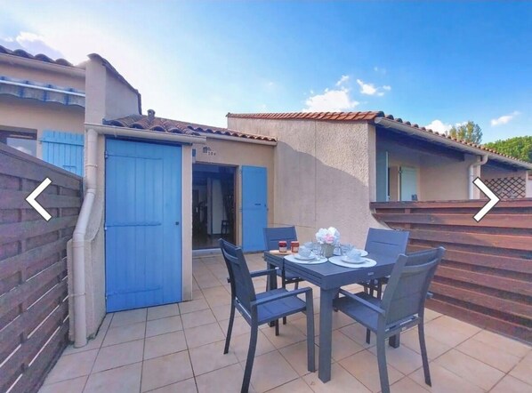 A patio with a table set for four, a blue door, and a small covered area.