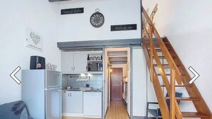 A compact living space with a kitchenette, a sofa, a wooden ladder, and a staircase leading to an upper level.