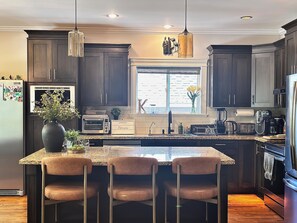 A kitchen with dark wood cabinets, a granite countertop, a built-in oven, a toaster, and a coffee maker. - LUX 4 Bedroom, 2 Bath Modern Farmhouse - Bear Mountain, Victoria, BC - Sleeps 8 (Victoria)