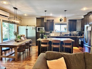 A modern kitchen with a central island, dark wooden cabinets, and a dining area with a wooden table and chairs. - LUX 4 Bedroom, 2 Bath Modern Farmhouse - Bear Mountain, Victoria, BC - Sleeps 8 (Victoria)