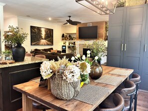 A modern kitchen with a wooden island, dark cabinetry, and a dining area with a table set for four. - LUX 4 Bedroom, 2 Bath Modern Farmhouse - Bear Mountain, Victoria, BC - Sleeps 8 (Victoria)