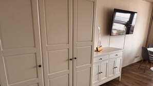 A room with a large wardrobe, a small table with chairs, and a TV mounted on the wall. - Sea view in the Meerzeitliebe Fehmarn (Fehmarn)