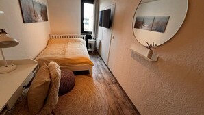 A bedroom with a bed, a bedside lamp, a round mirror, and a small shelf with a plant. - Sea view in the Meerzeitliebe Fehmarn (Fehmarn)