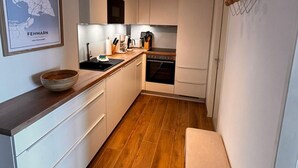 A compact kitchen with white cabinets, a wooden countertop, a built-in oven, and a wall-mounted light fixture. - Sea view in the Meerzeitliebe Fehmarn (Fehmarn)