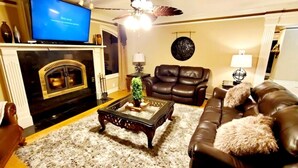 Una sala de estar con chimenea, sofá de cuero y televisión.