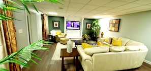 A living room with a sofa, armchairs, a coffee table, a television, and a plant. - Lakefront Luxury Estate w/ Pool, Bar & 2 Acres (Conyers)
