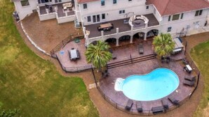 Una casa grande de dos pisos con piscina, mobiliario exterior y un patio cercado.