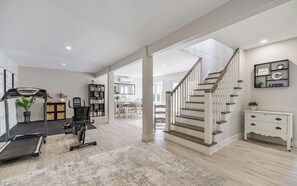 A spacious living area with a treadmill, exercise bike, and a staircase leading to an upper level.