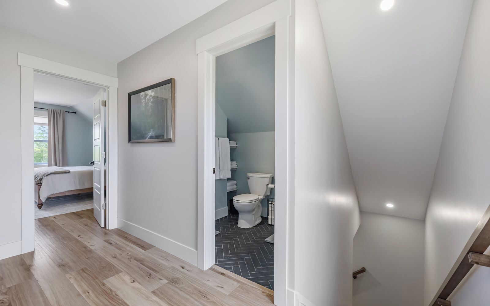 A modern interior with a wooden floor, a bed, a bathroom with a toilet, and a staircase.