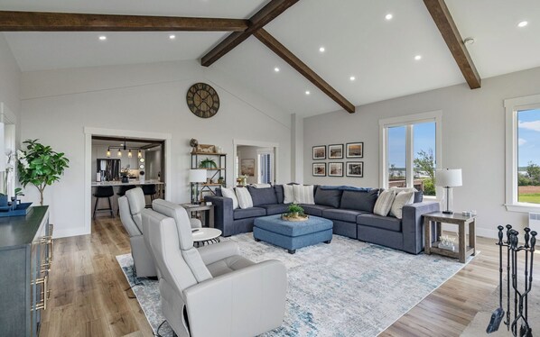 A spacious living room with a large sectional sofa, a coffee table, and a dining area with a kitchen in the background.
