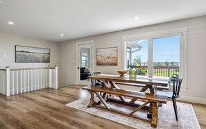 A spacious room with a wooden dining table, benches, and a view of the outdoors through large windows. - Spacious 6 BR Water view home - Sleeps 11 - Private - Near beach (Mount Stewart)