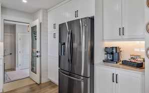 A modern kitchen with white cabinetry, a stainless steel refrigerator, and a coffee maker on the countertop.