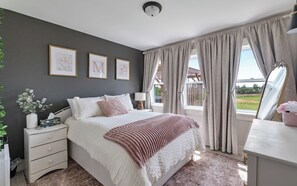 A bedroom with a bed, bedside table, lamp, curtains, and framed pictures on the wall.