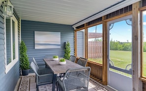 A covered patio with a table and chairs, a view of the backyard, and a wooden door.