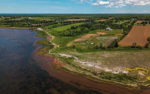 Une vue aérienne d’un paysage côtier, avec des champs, une rivière et quelques bâtiments dispersés.