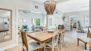 Un'ampia sala da pranzo con tavolo e sedie in legno, un lampadario intrecciato e vista sulla spiaggia attraverso un'apertura.