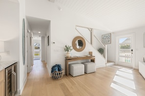 A modern interior with a wooden staircase, a console table with a mirror, and a basket with clothes. - New AMI Retreat | Private Pool | Walk to Beach (Anna Maria)