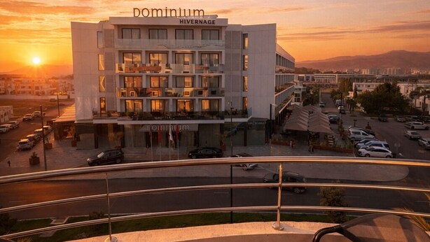 Ein modernes Hotel mit Dachterrasse und Blick auf eine Stadtlandschaft bei Sonnenuntergang.