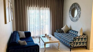 Ein modernes Wohnzimmer mit einem blauen Sofa, einem gemusterten Sofa, einem Glastisch und einem dekorativen Spiegel an der Wand.
