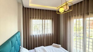Ein Hotelzimmer mit einem modernen Bett, einem Kopfteil, einem Fenster mit Vorhängen und einer Pendelleuchte.