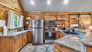 Een moderne keuken met houten wanden, roestvrijstalen apparatuur, granieten aanrecht en een groot raam.