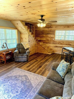 A cozy cabin interior with a wooden staircase, a sofa, a chair, and a ceiling fan. - Little River Hideout - Two Cabins on Little River (Cedar Bluff)