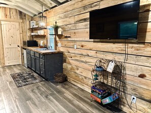A kitchen with wooden walls, a flat-screen TV, and a coffee machine. - Little River Hideout - Two Cabins on Little River (Cedar Bluff)
