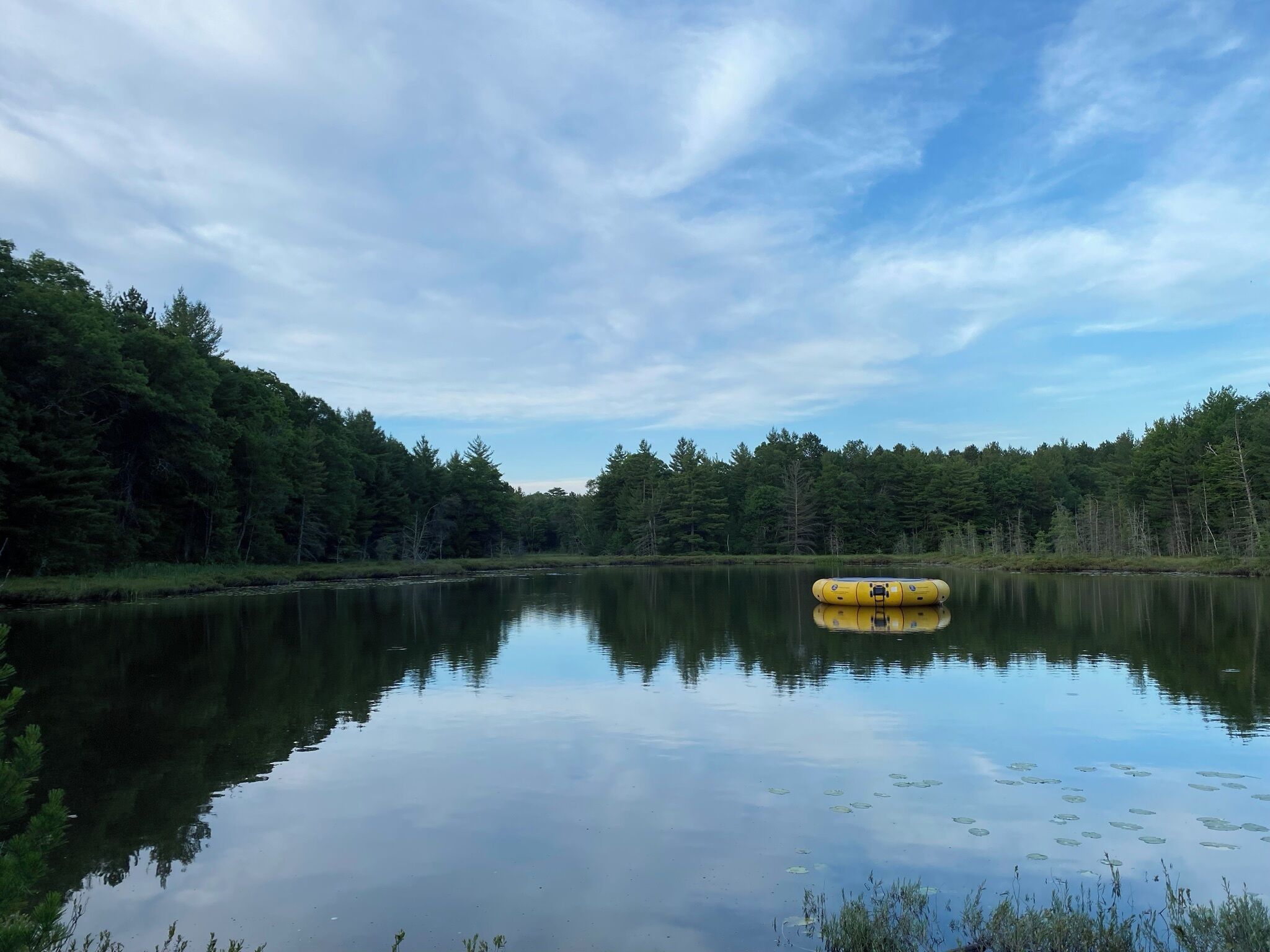 Um lago calmo com uma bóia amarela no centro, rodeado por uma floresta densa.