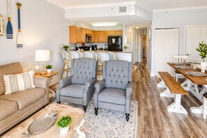 A living room with a sofa, two armchairs, a coffee table, and a dining area with a table and benches. - Waterfront Beach Condo With Pool & Jacuzzi (Treasure Island)