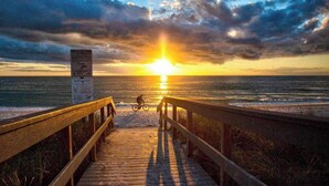 Un muelle de madera que conduce a la playa con un atardecer de fondo.
