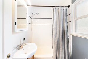 Ein Badezimmer mit weißem Waschbecken, einem Spiegel, einer Dusche und einem Duschvorhang.