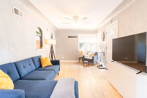 A living room with a sofa, a TV, a ceiling fan, and a window. - Cozy Townhome Steps from City Park - Pet-Friendly Monthly Stays (Denver)