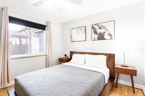 Ein Schlafzimmer mit einem Bett, einem Nachttisch, einer Lampe und zwei an der Wand befestigten Kunstwerken.
