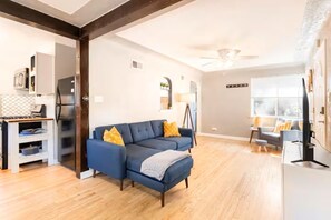 A modern living room with a blue sofa, wooden flooring, and a dining area with a table and chairs. - Cozy Townhome Steps from City Park - Pet-Friendly Monthly Stays (Denver)