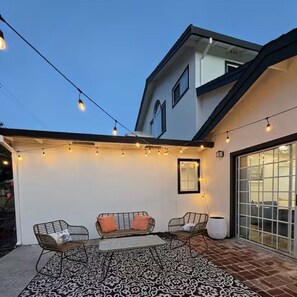 A patio with a patterned rug, two metal chairs, a sofa, and string lights.