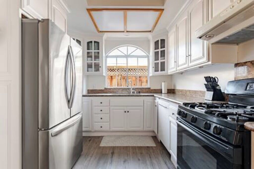A kitchen with white cabinetry, a stainless steel refrigerator, a gas stove, and a window with a lattice design.